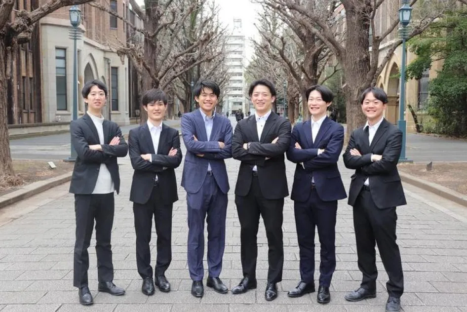 屋外の並木道で腕を組み並んで立つ、スーツやジャケットを着用した若い男性6人のグループショット。